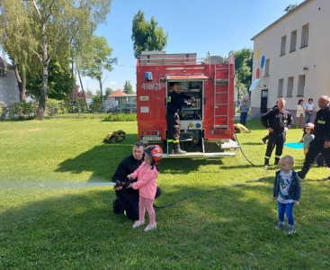 Na zdjęciu dziewczynka trzyma wąż strażacki i leje wodą. - powiększ