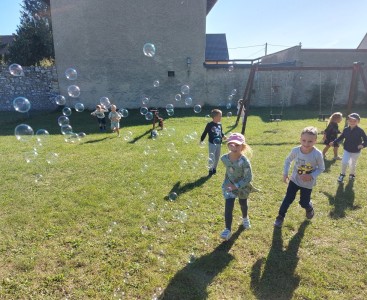 Zdjęcie przedstawia dzieci podczas łapania baniek na placu zabaw. - powiększ