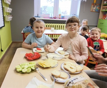 Zdjęcie przedstawia dzieci w trakcie przygotowania kanapki.  - powiększ