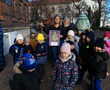 Na zdjęciu dzieci wręczają kartkę bożonarodzeniową  - powiększ