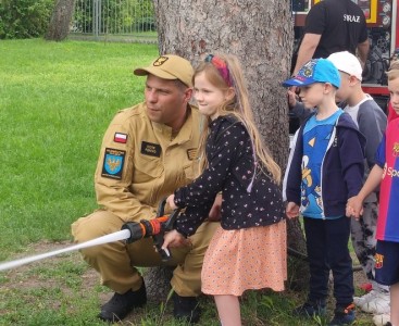 Zdjęcie przedstawia dziecko w trakcie lania wody z węża strażackiego - powiększ