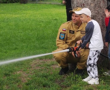 Zdjęcie przedstawia dziecko w trakcie lania wody z węża strażackiego - powiększ